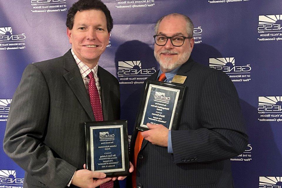 Mark Kovacs and Gary Leising hold up plaques at the Genesis Group's Celebration of Education event in November 2023.